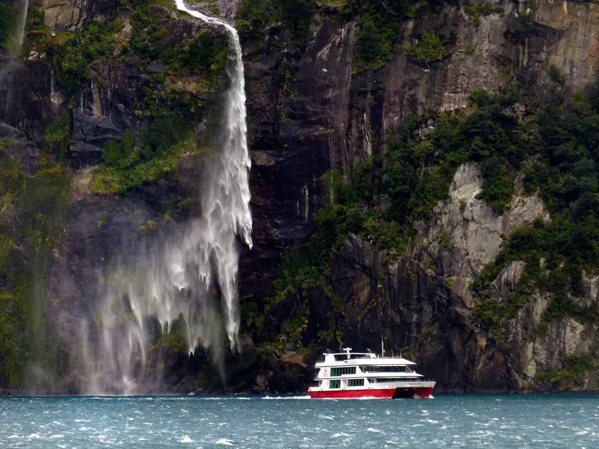 A cruise boat below a waterfall in Milford Sound